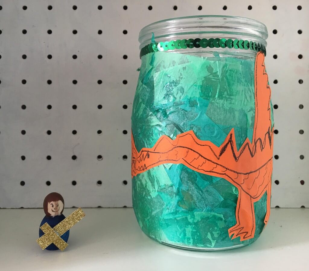 St George's Day isn't celebrated until April 23rd but that didn't top us having fun with this George and the Dragon luminary. We really enjoy crafting with these large glass jars and now the children are a little bit older I don't worry about them so much. Saint George lived in the 3rd century and was born in what was the Roman Empire, somehow he ended up as the patron Saint of England Supplies needed to make a St George and the dragon luminary Clip top glass jar with clip-top lid removed Bostik White Glu Green tissue paper wooden peg doll blank acrylic paint dragon craft supplies St George and the Dragon luminary I mixed a healthy dollop of the Bostik White Glu with a small amount of warm water. My 4 year old cut the green tissue paper into small pieces. then she carefully painted the glue onto the jar and covered it with pieces of tissue paper. St George and the Dragon craft We used two shades of green and she made two layers. We set the glass jar aside to dry. St George and the Dragon craft My 5 year old drew this fantastic picture of a dragon on a sheet of orange paper. I love this drawing and think he has captured everything from the smoke coming out his nostrils to his scaly skin. I carefully cut around his drawing then we glued it to our jar with more of the Bostik White Glu. st georges dragon I painted a small wooden peg doll to look like St George and added a mini sword from some gold glittery card. Then we were ready to create our dragon scene - St George fighting off the dragon and earning his place in history! My children were fascinated by the story and this is a great way to teach them about our patron saints with a fun craft activity.