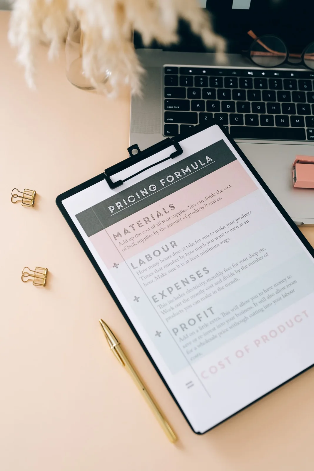 A clipboard with a printed pricing form and stationery beside a laptop