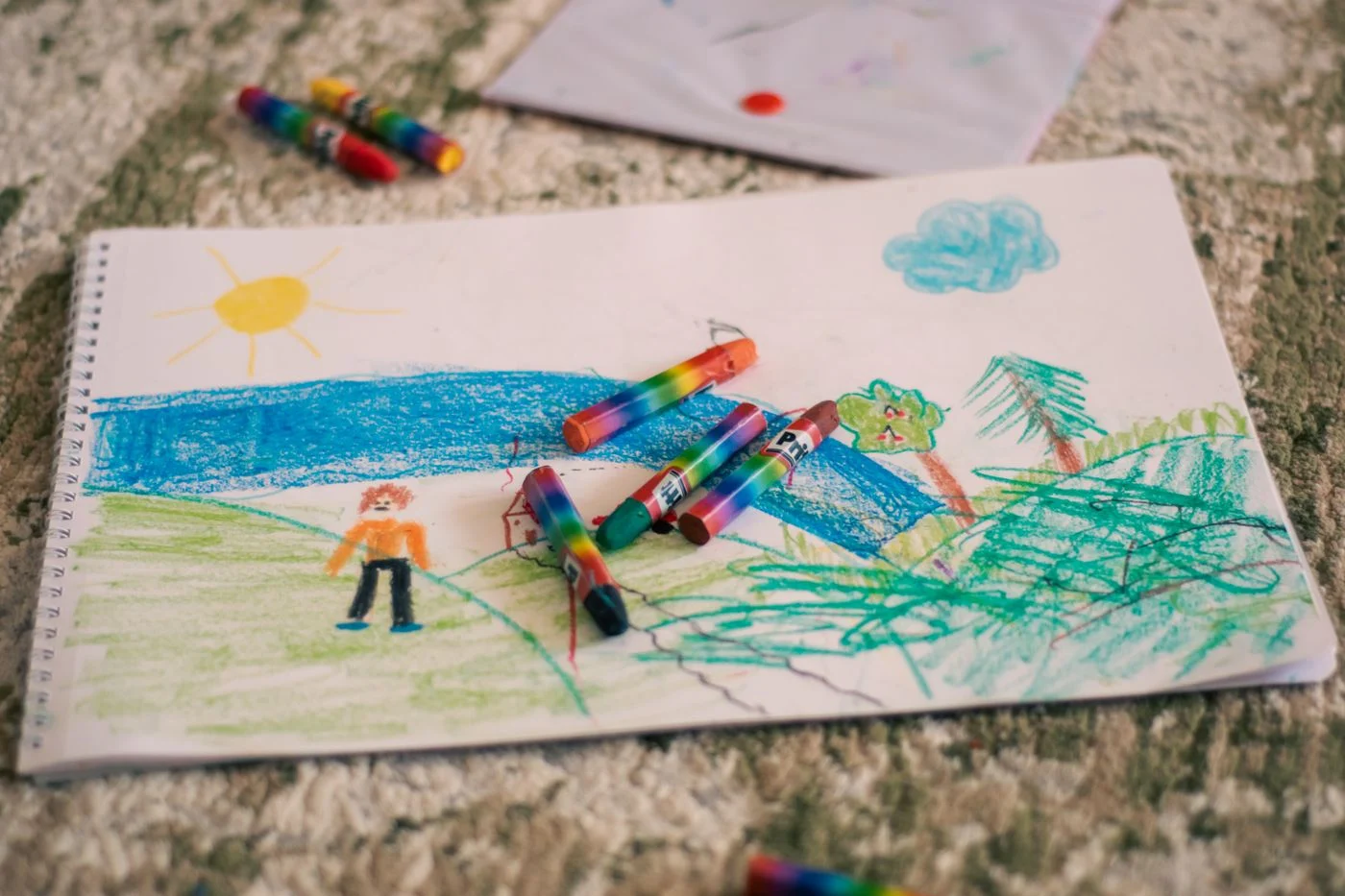 Colorful landscape drawing with crayons scattered on paper