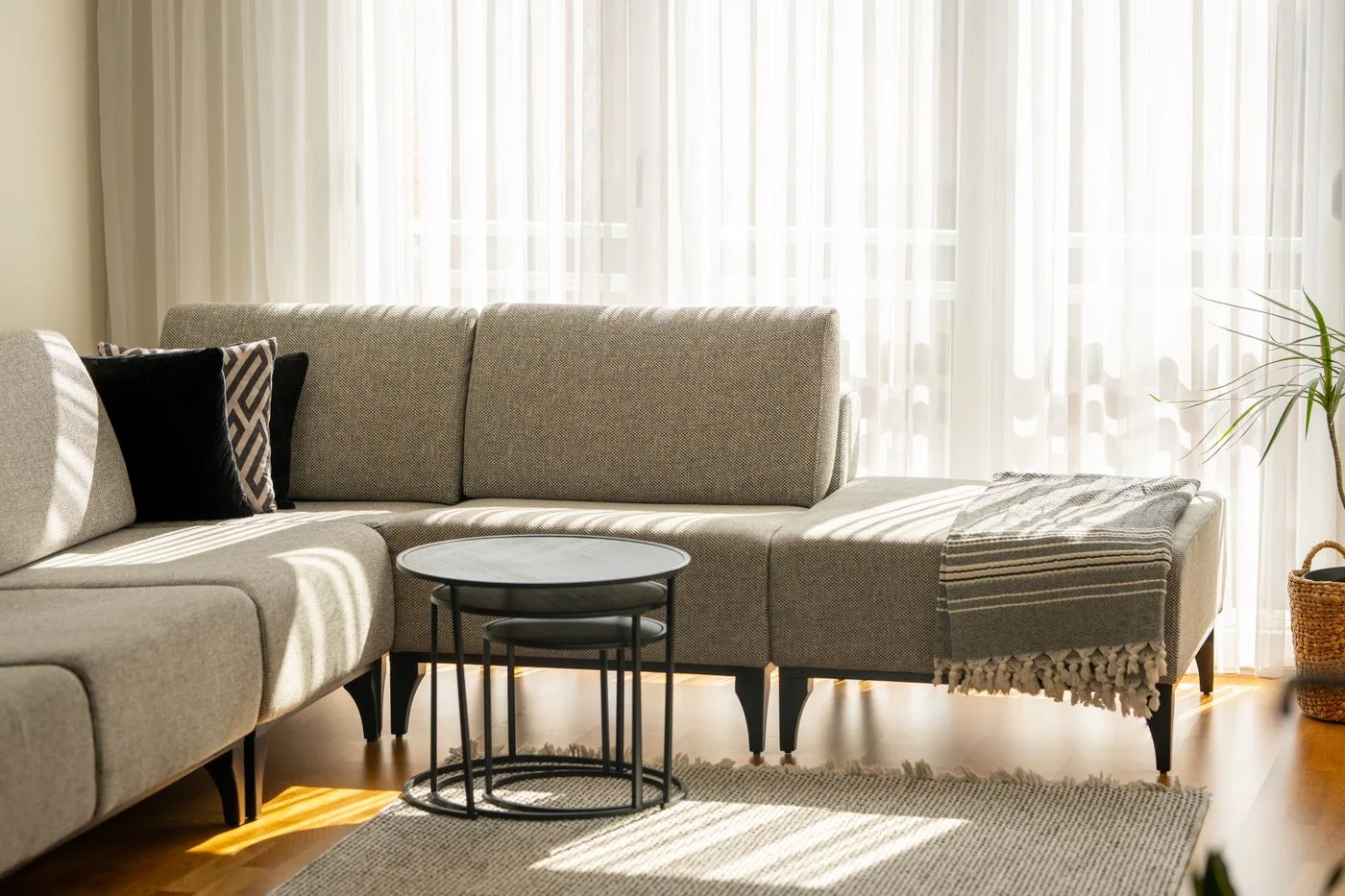 A pale sectional sofa and round nesting tables beside sheer curtains