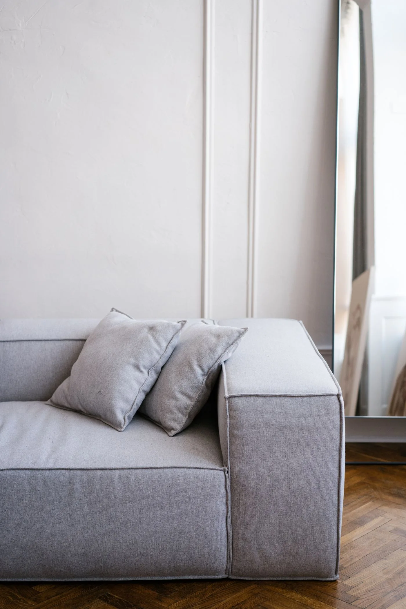 A gray sofa with pale cushions beside a light wall